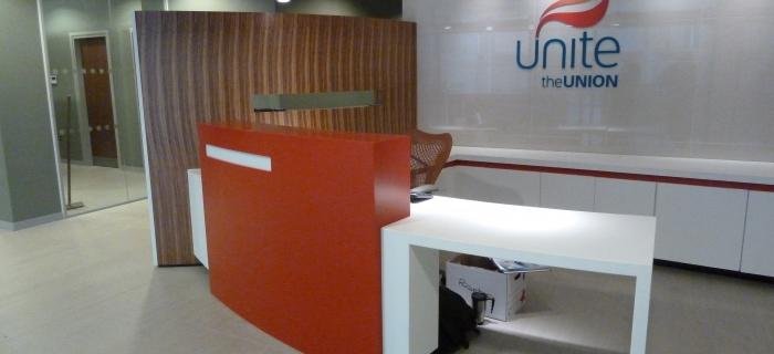 Unite the Union Reception Desk – Liverpool Manufactured from corian using hot and glacier white . Rear cupboards and worktops including doors manufactured from glacier white corian with hot (RED) inlay band. Curved laminated privacy screen wall made up from mdf and laminated in zebrano formica and a curved glass vision panel . 